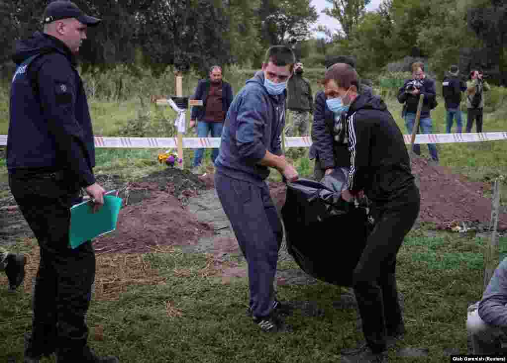 Мужчины несут тело человека, который, по данным украинской полиции, был убит российскими веонными в Балаклее