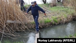 Қарақошқыл суынан төңірекке сасық иіс тарап жатқан өзеннің үстінен өткел ретінде тасталған тақтаймен әупірімдеп өтіп жатқан адамдар. Талғар ауданы, Алматы облысы, 18 сәуір 2021 жыл.